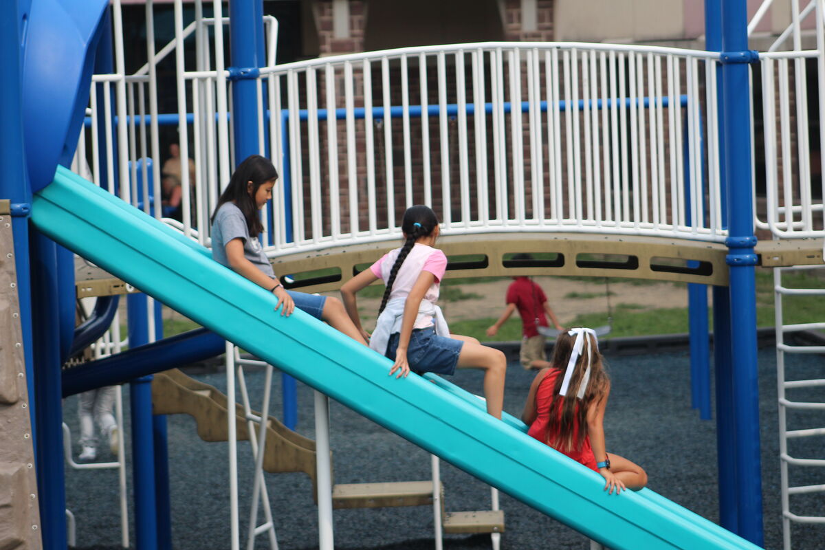 Children play on a blue slide at a playground, enjoying the outdoors.