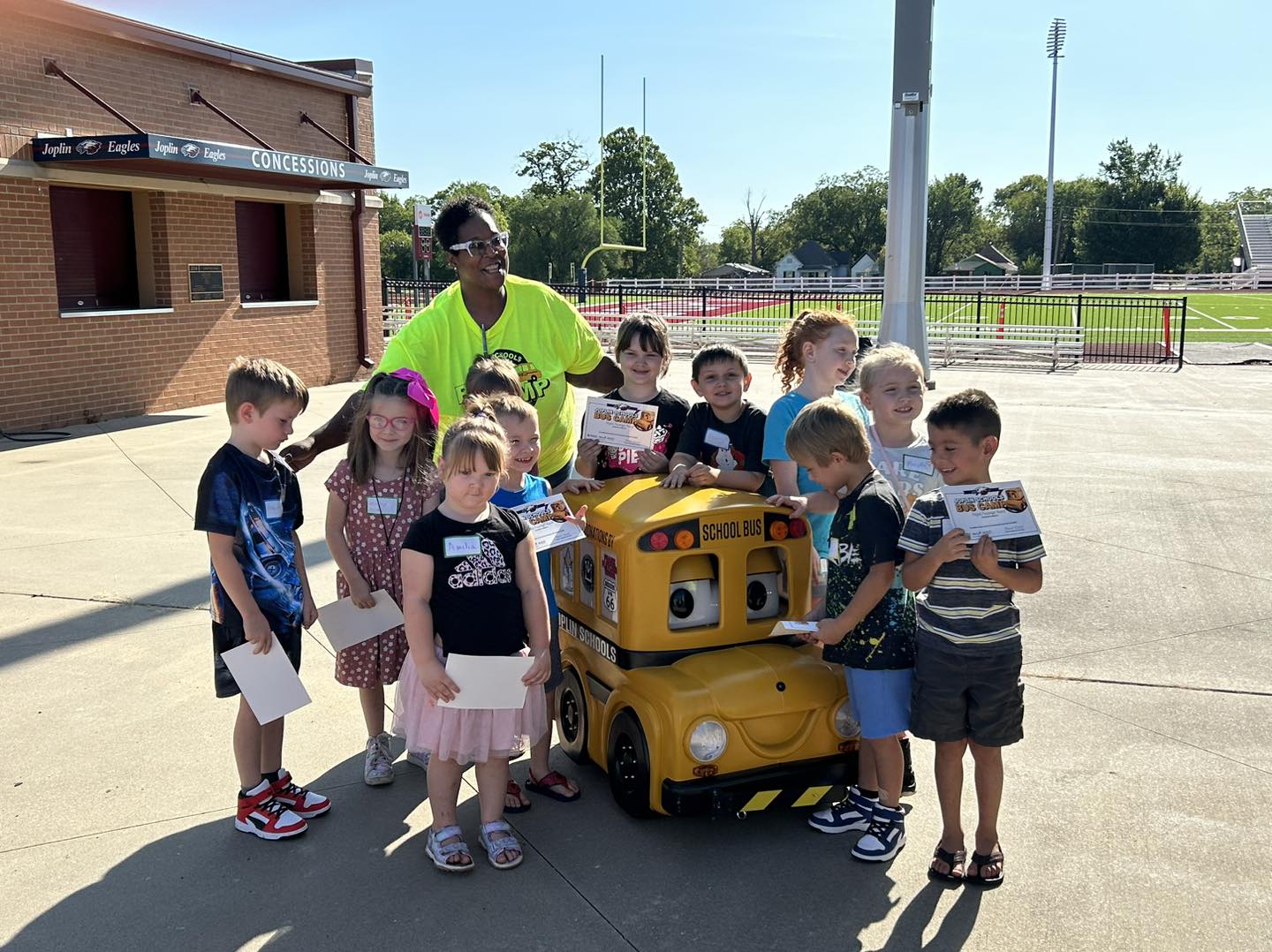 A group of small children pose around Buster the Talking School bus at bus camp