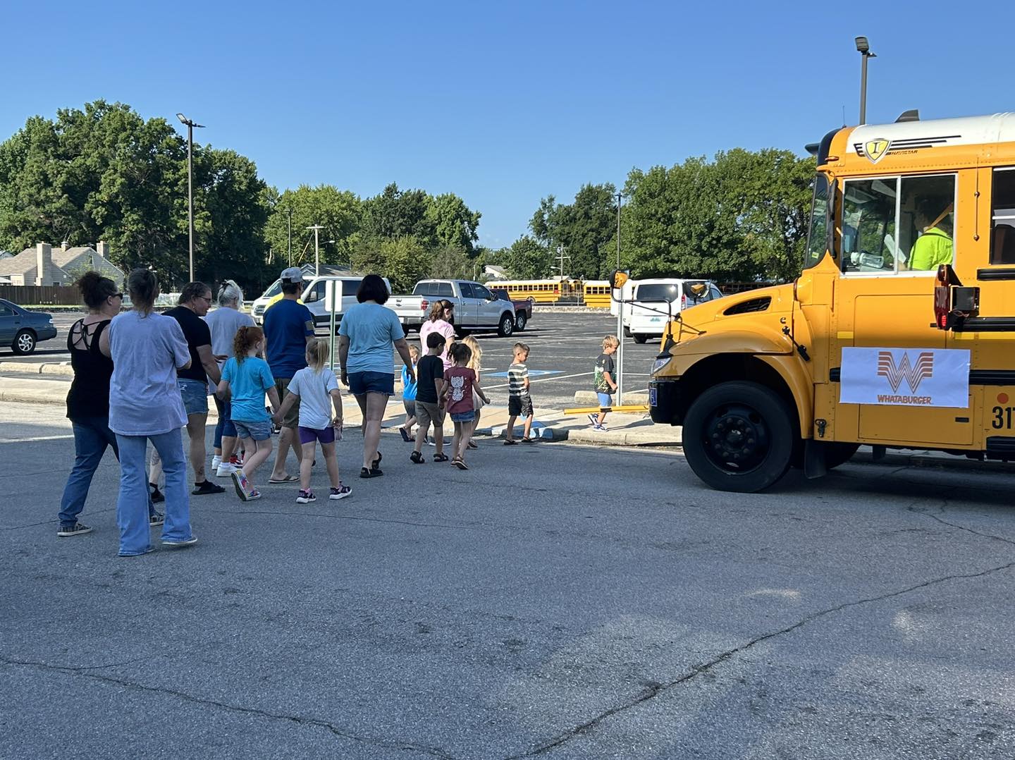 A line of children and parents wait to cross the street and load onto a waiting school bus.