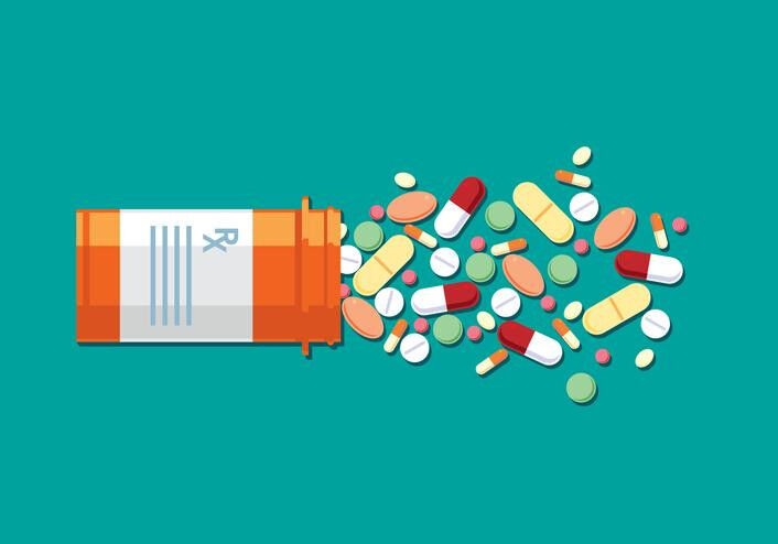 An orange prescription bottle spills out a variety of colorful pills.