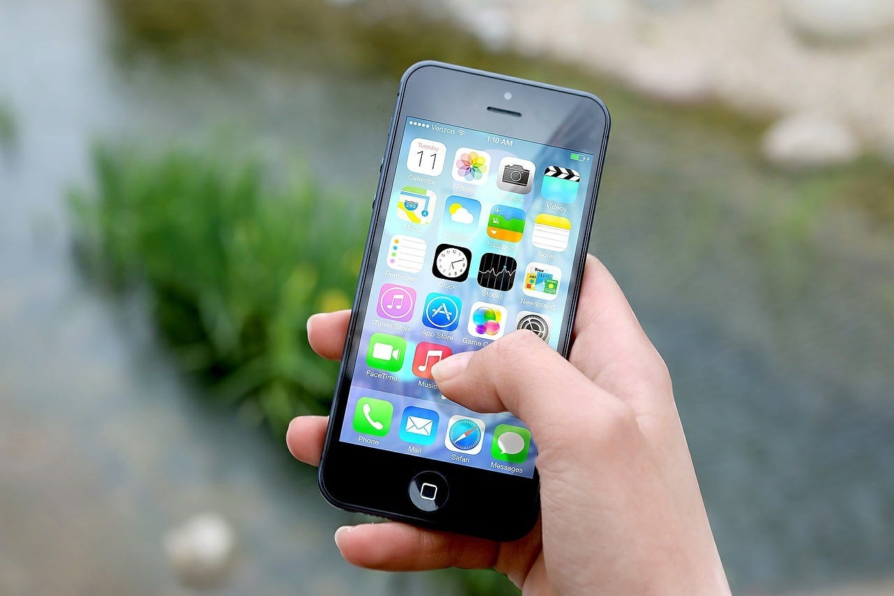 A hand holds a smartphone with various app icons displayed on the screen.