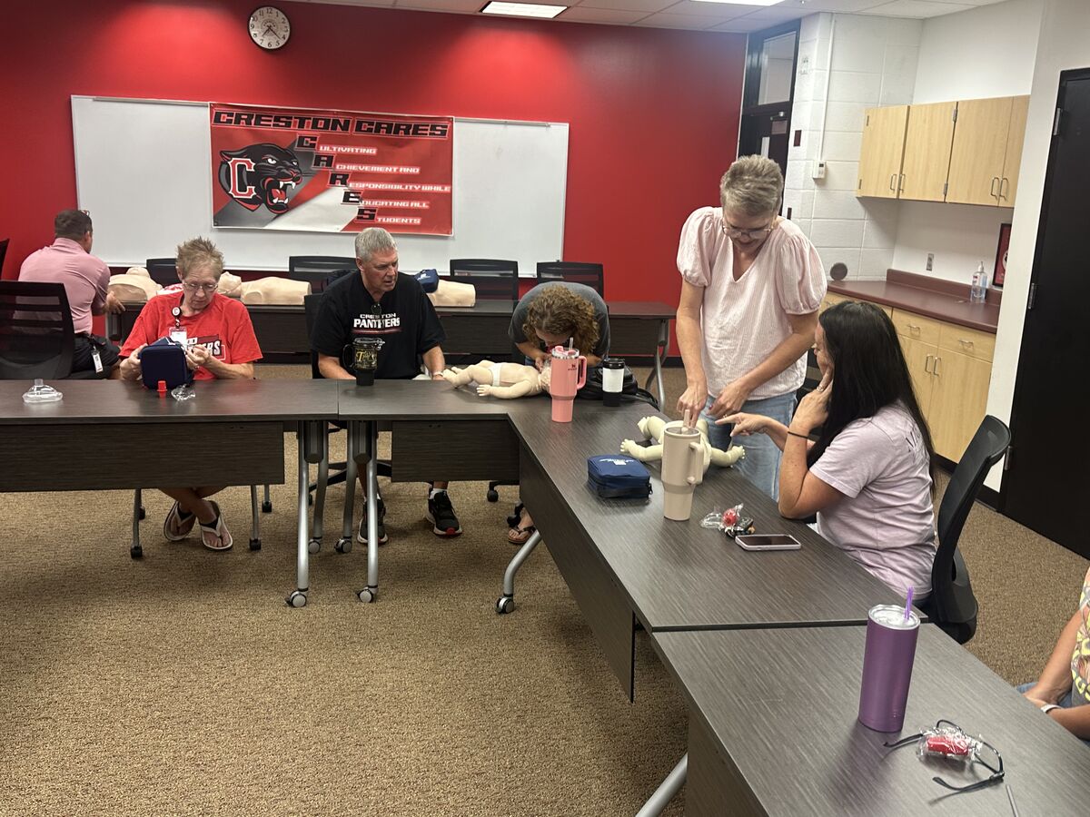 A group of people participate in a first aid training session, using mannequins.