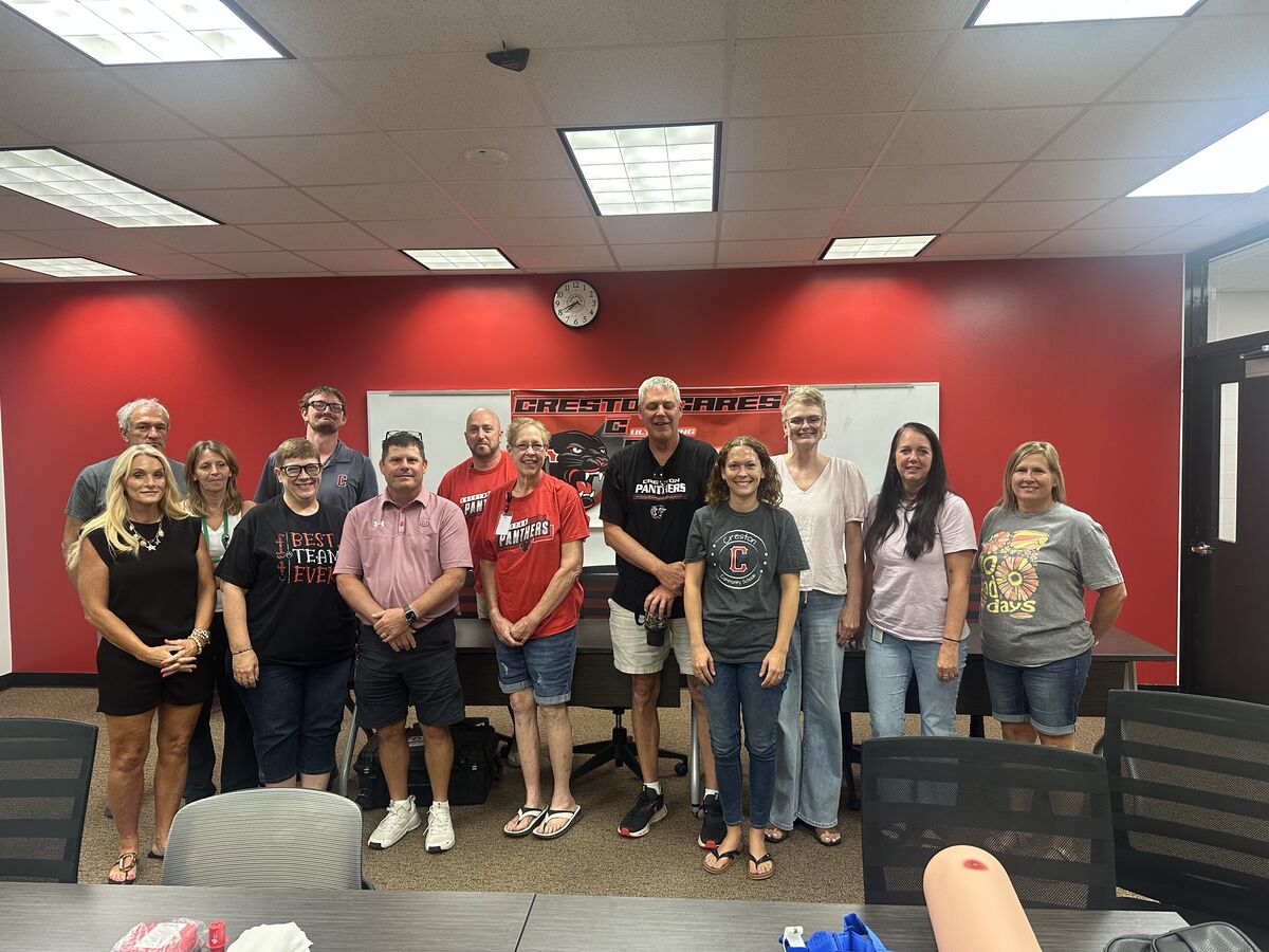 A group of people stand together in a room with a red wall and a whiteboard.
