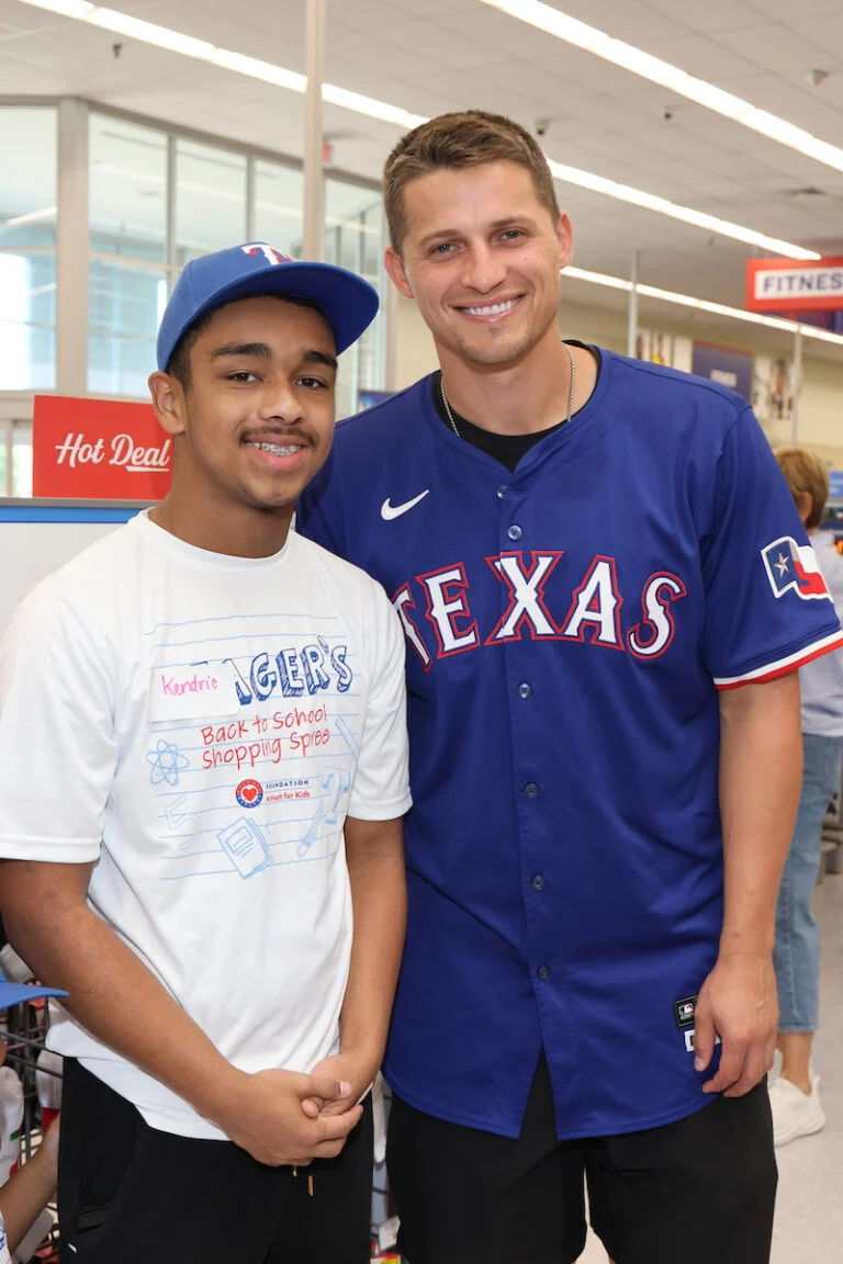 Two men smile for the camera in a store setting, one wearing a baseball jersey.