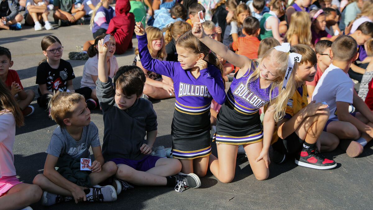 A group of children sit on the ground, some holding up small cards.