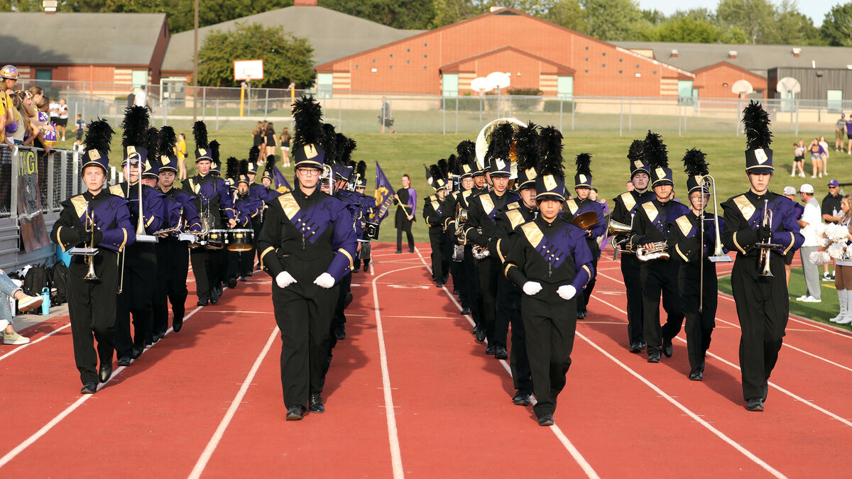 A marching band in purple and black uniforms performs on a red track.