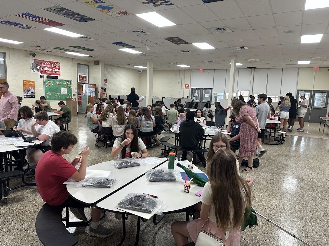 Students gather in a school cafeteria, some eating and working.