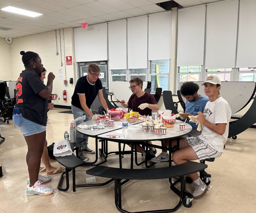 A group of young people prepare and serve treats at a table.