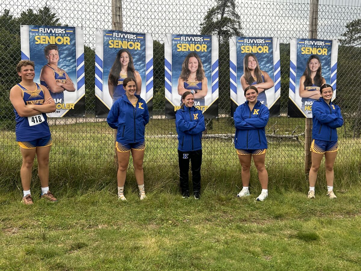 A group of cross country seniors pose in front of banners, wearing team uniforms.