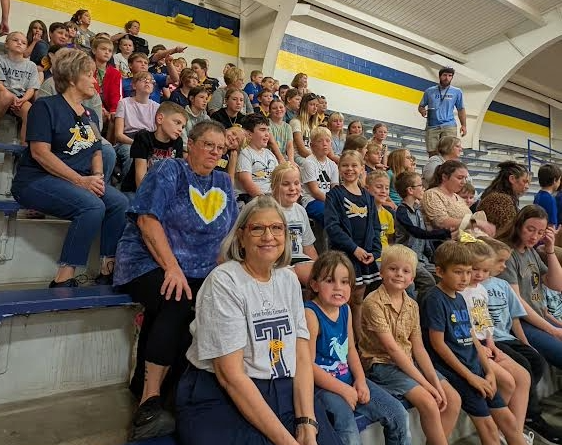 A group of people, including children and adults, sit in bleachers at an event.