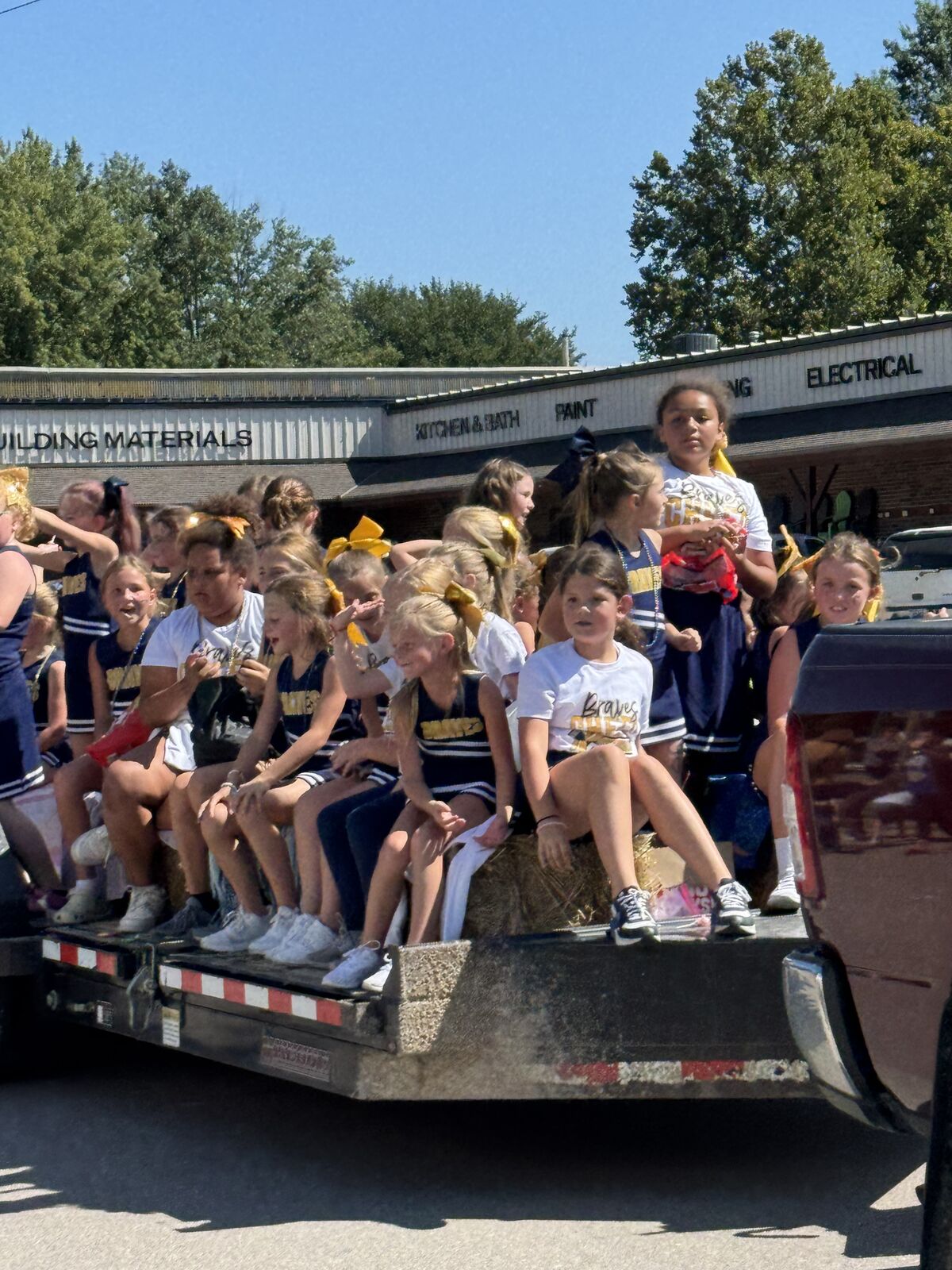 A group of cheerleaders ride on a float, smiling and waving.