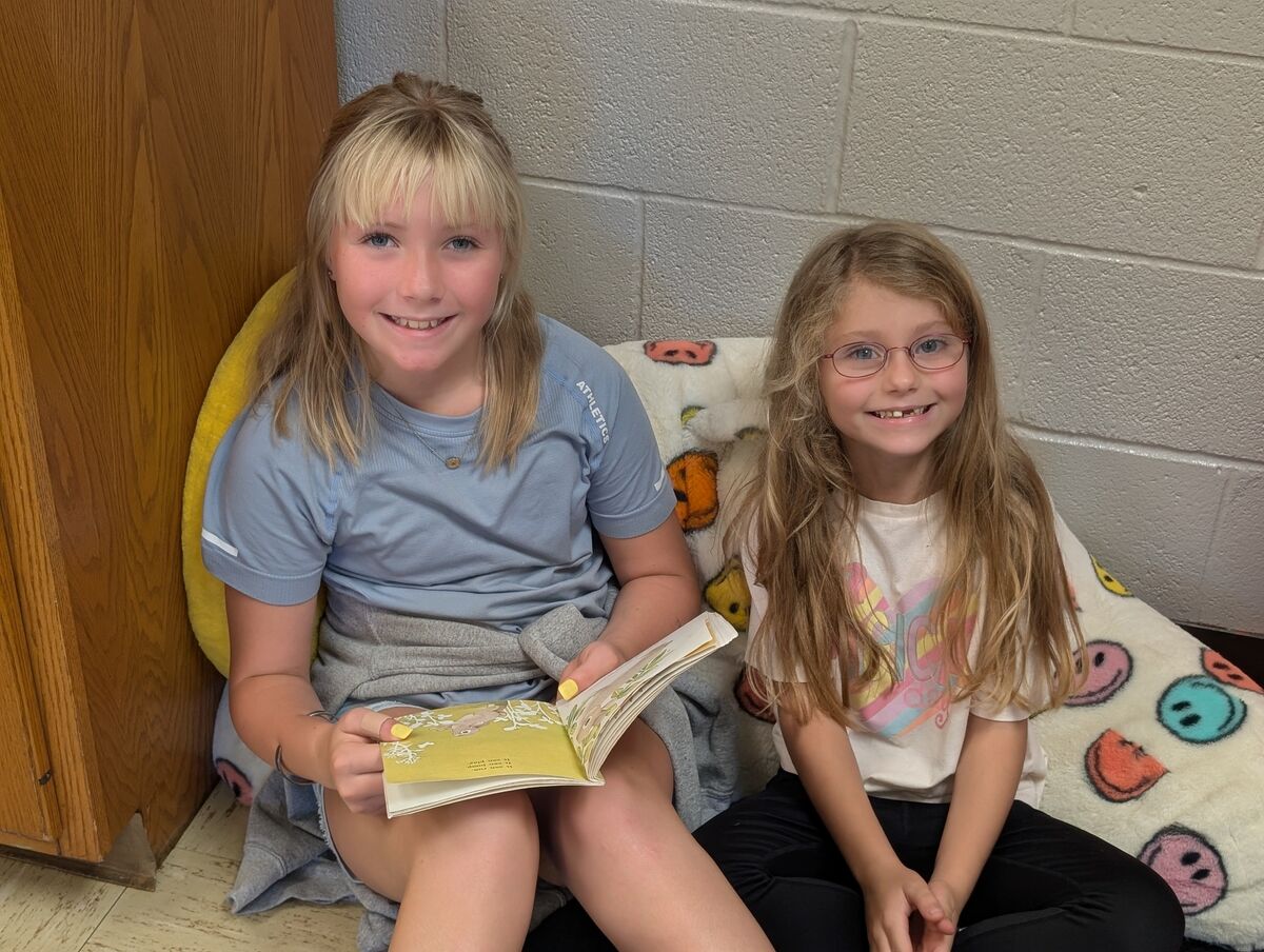 Two young girls smile while sitting and reading a book together.