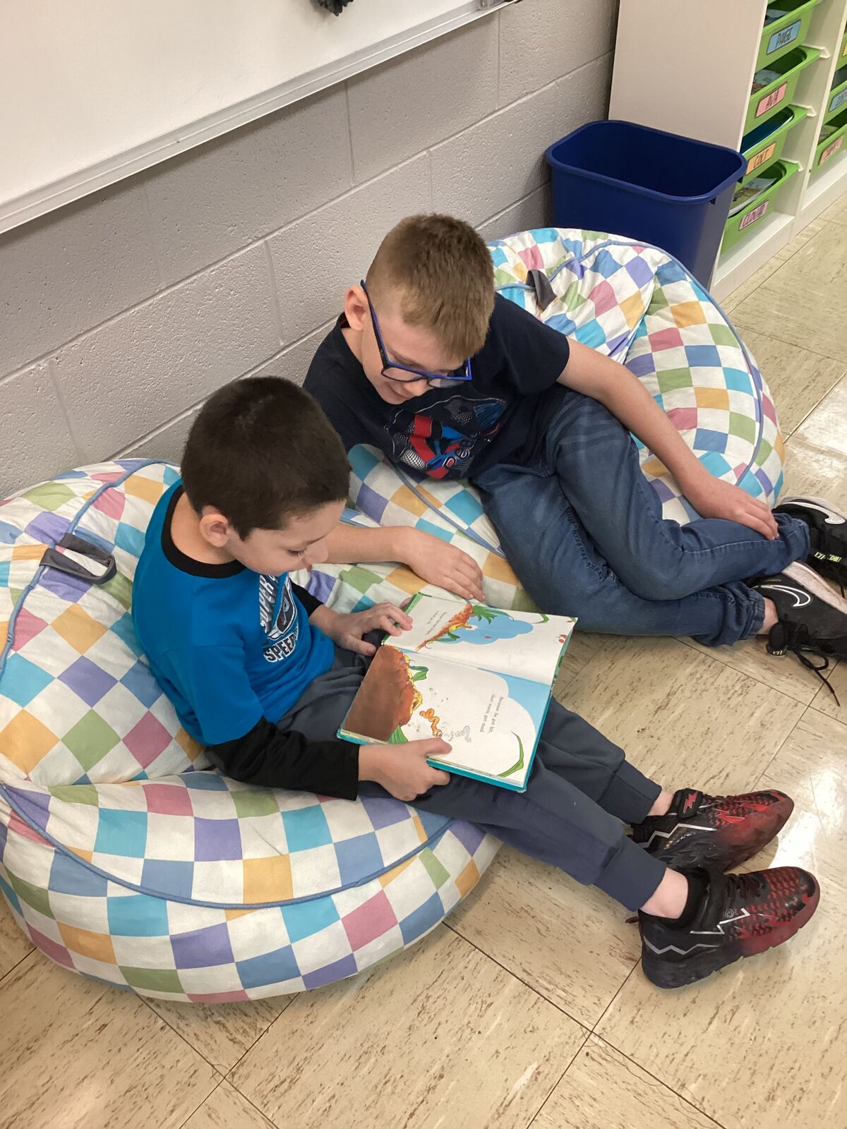 Two children read a book together while relaxing on beanbag chairs.