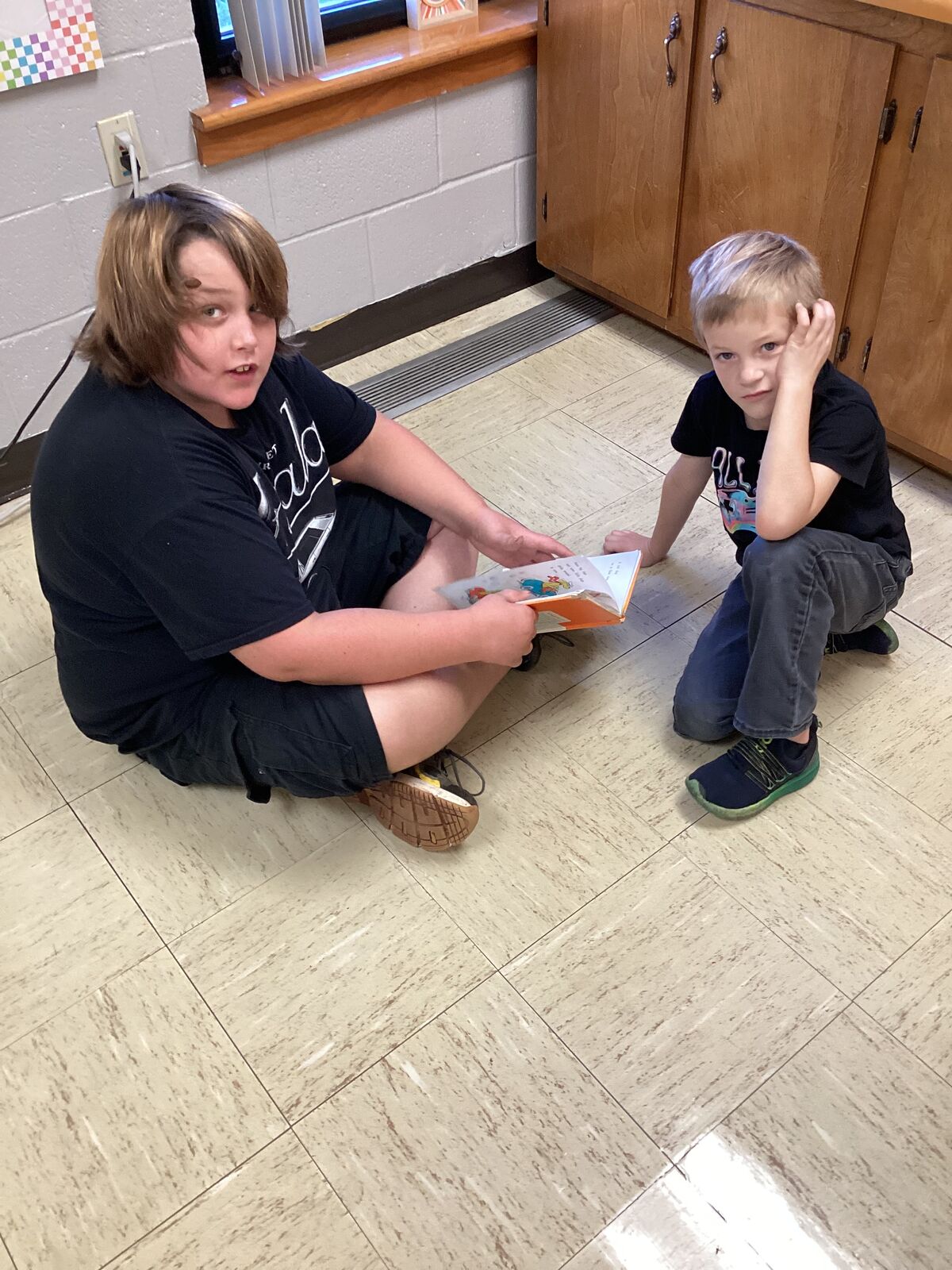 Two children are reading a book together on a tiled floor.