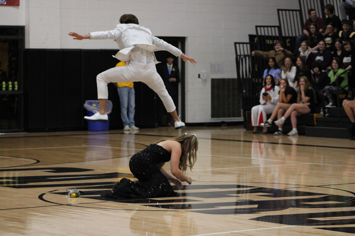 A person in a white suit leaps over a person in a black dress on a basketball court.