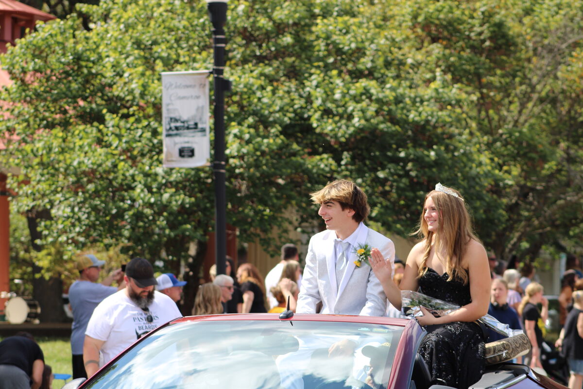 Sophomore royalty wave from a convertible during a parade, smiling at the crowd.