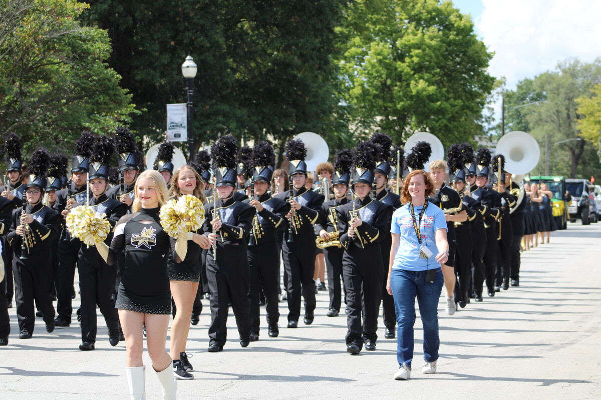 A marching band parades down a street, accompanied by cheerleaders.