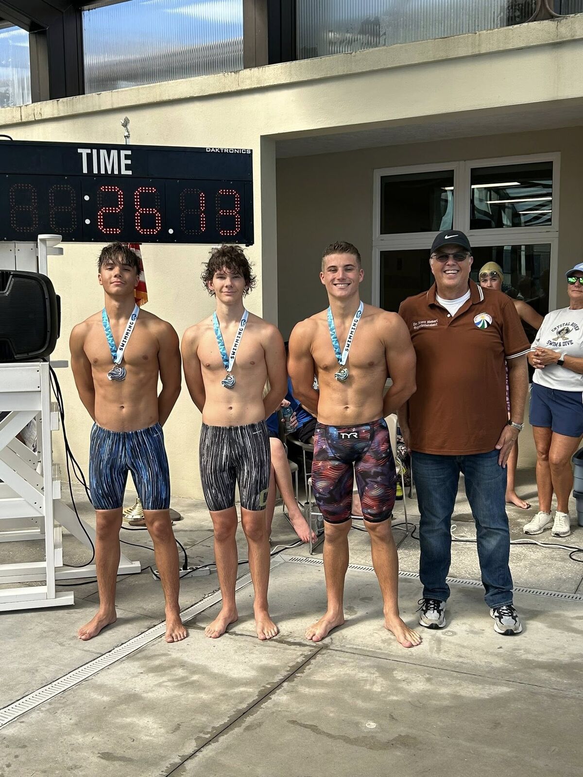 Three swimmers stand proudly with medals, posing for a photo after a competition.