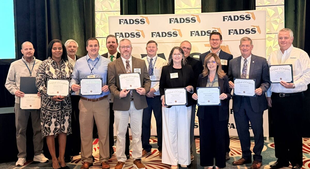 A group of people stand together, holding certificates in front of a FADSS banner.