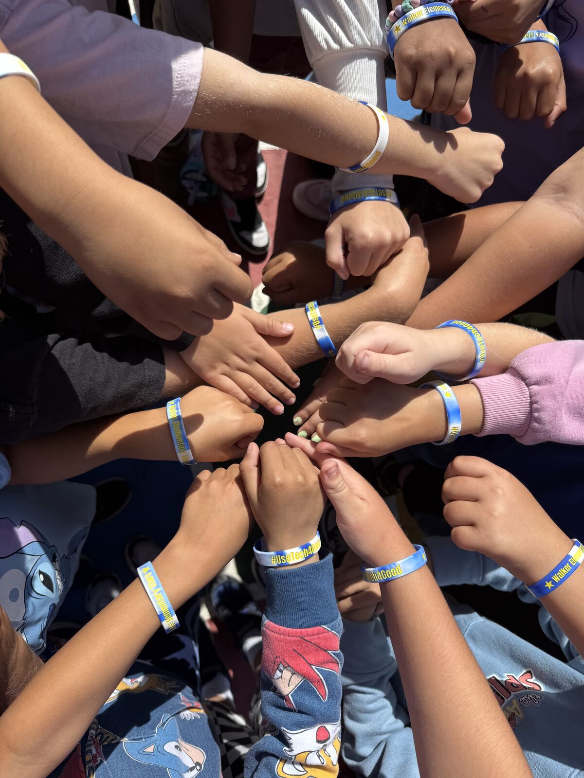 A group of children's hands are joined together in a circle, wearing matching wristbands.