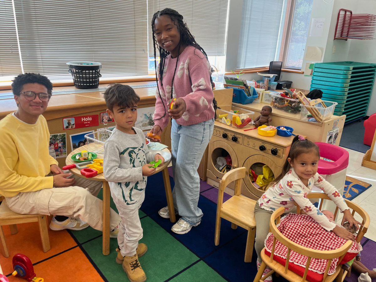 Children and adults play with toys in a colorful classroom setting.