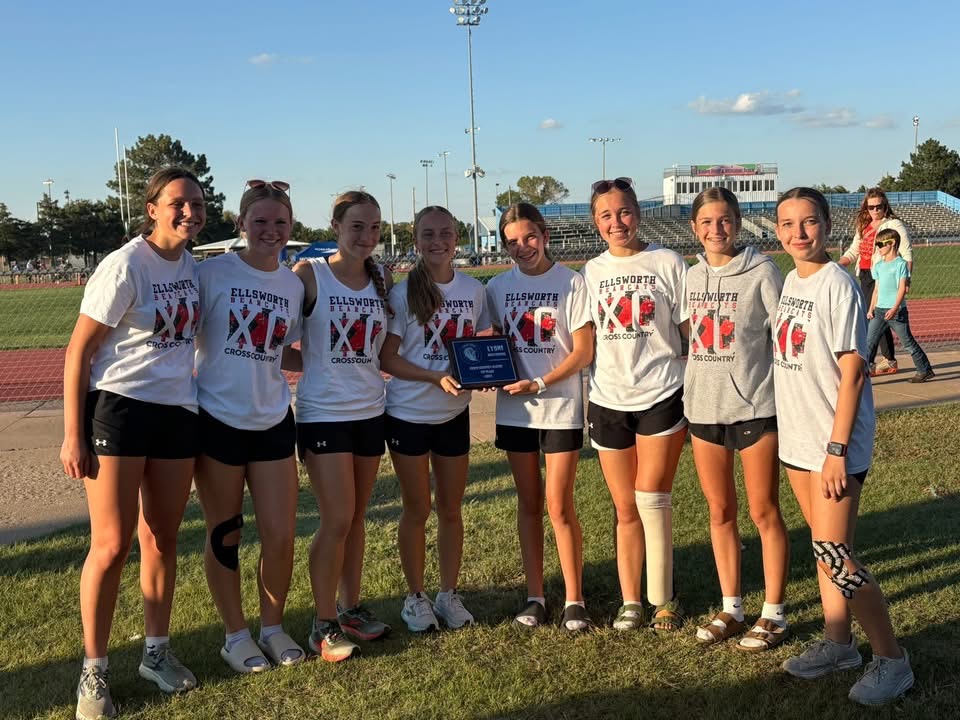 A cross-country team poses with a trophy on a grassy field.