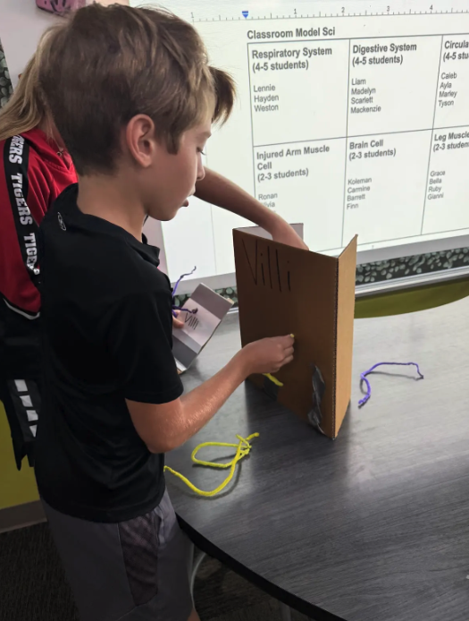 Two students work on a science project, using a cardboard model and colorful yarn.