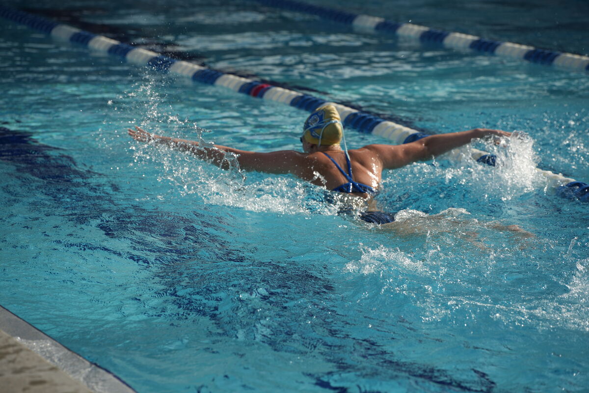 A swimmer in a blue swimsuit performs the butterfly stroke in a pool.