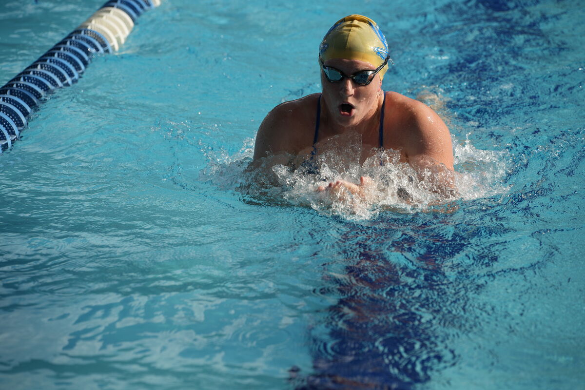 A swimmer in a yellow cap and goggles swims freestyle in a pool.
