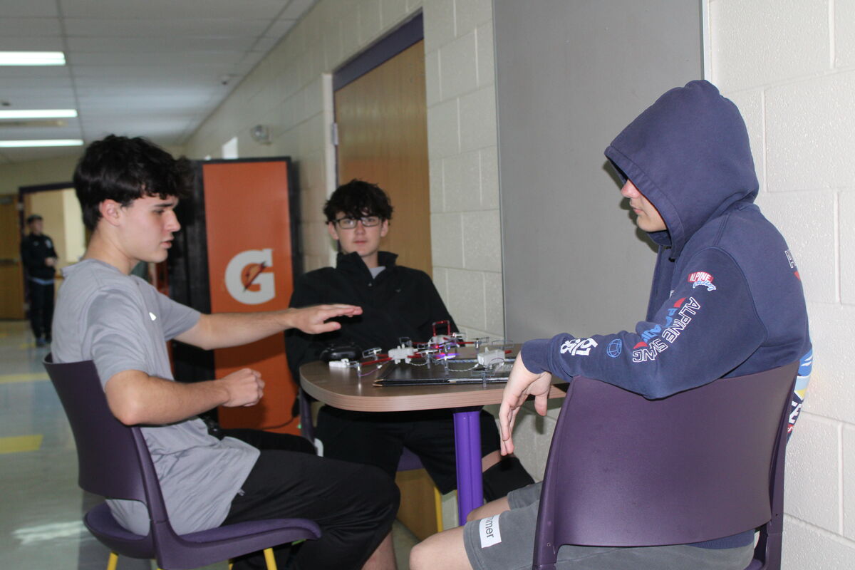 Three young people sit around a table, possibly working on a project.