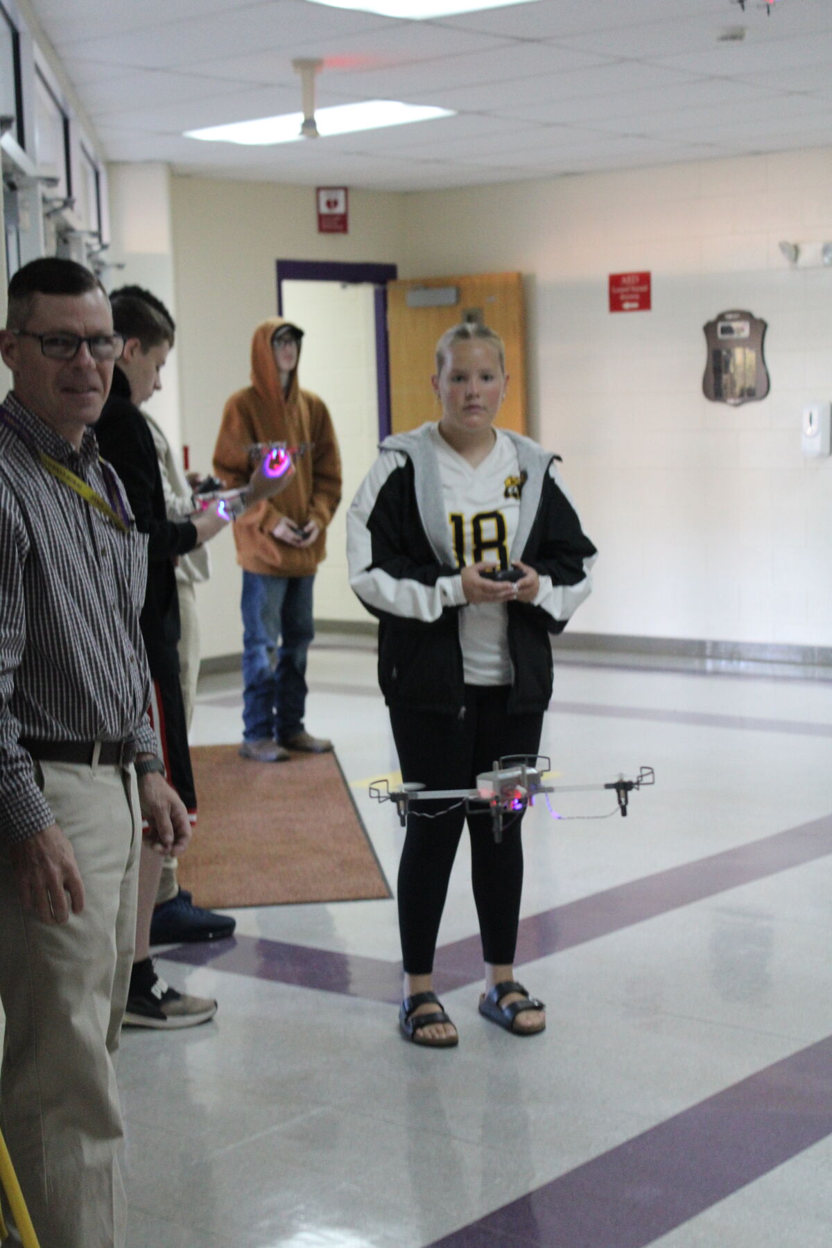 Students and an adult are in a school hallway, some holding drones.