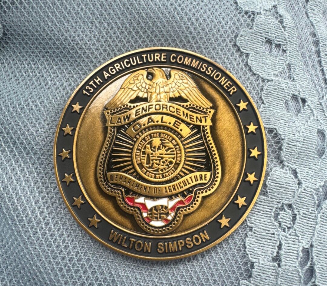 A gold and black coin with text and a seal, resting on a textured blue surface.