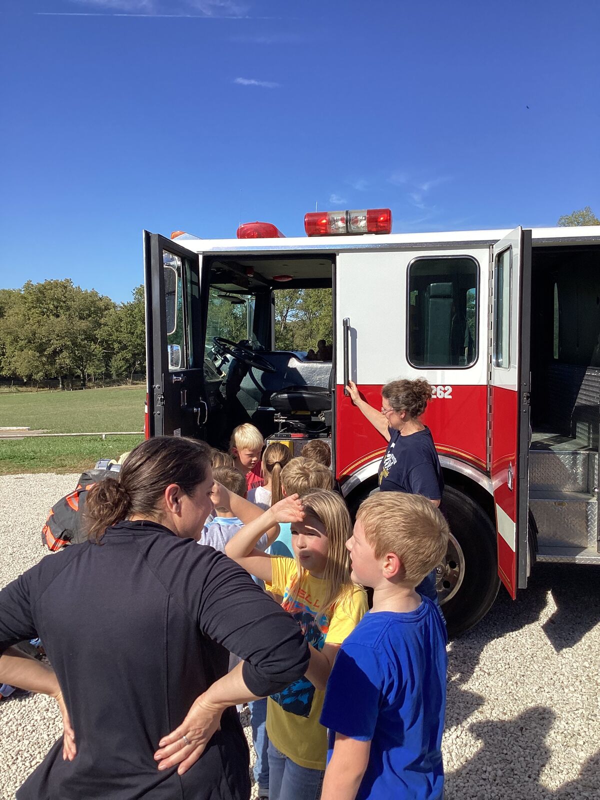 Children gather around a fire truck with adults, likely on a field trip.