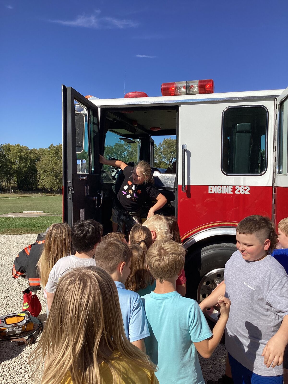 Children gather around a fire truck, with one child inside the cab.