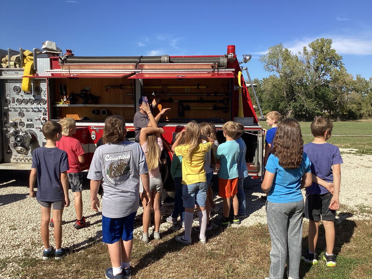 A group of children listens to a presentation in front of a fire truck.