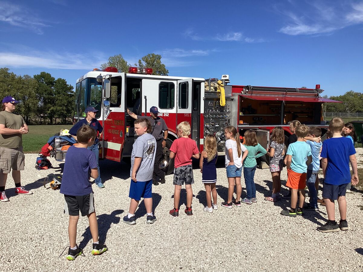 Children and adults gather around a fire truck on a sunny day.