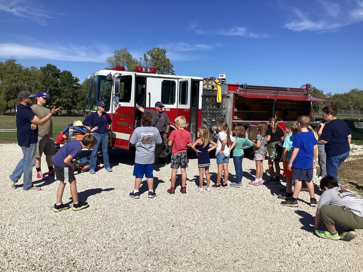 Children and adults gather around a fire truck on a sunny day.