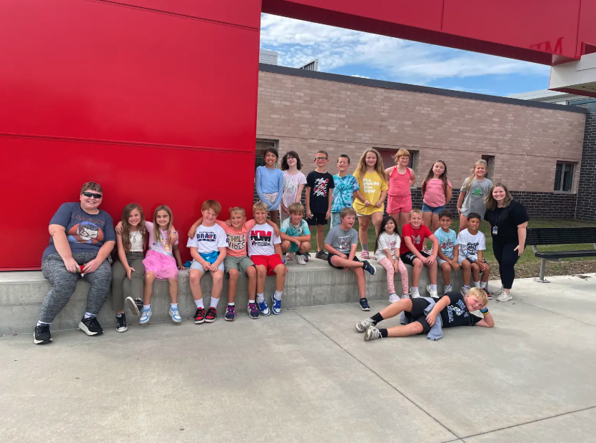 A group of children and two adults pose for a photo outside a building.