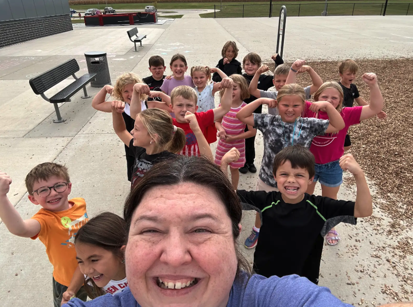 A group of children and an adult flex their muscles, smiling at the camera.