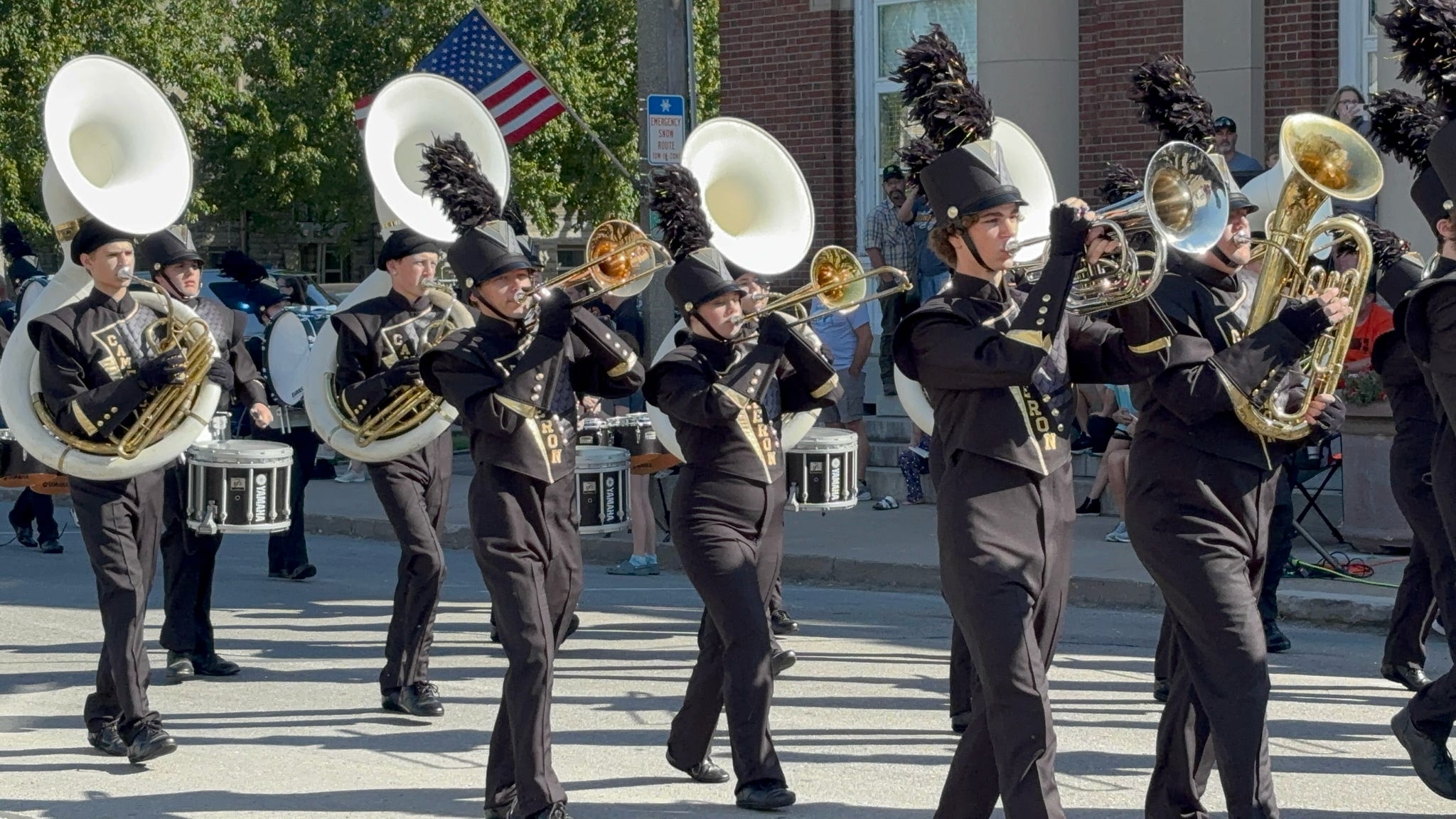 CHS band members in black uniforms play and march during a parade on a street