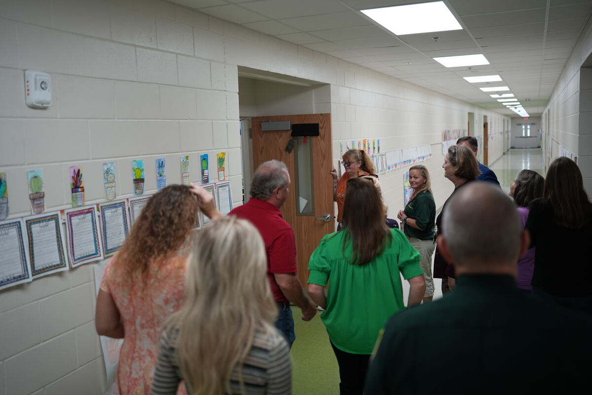 A group of people stand in a school hallway, looking towards a doorway.