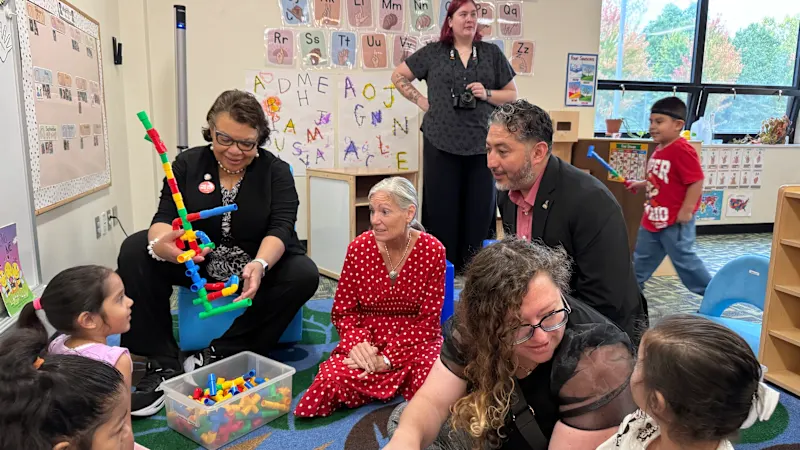 Adults interact with young students who are playing with plastic blocks
