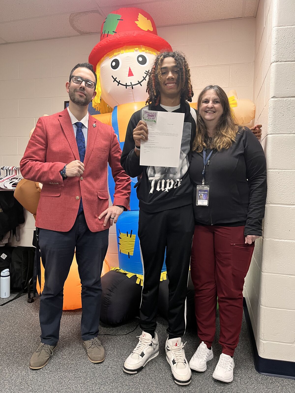 Three people pose for a photo with an inflatable scarecrow decoration.