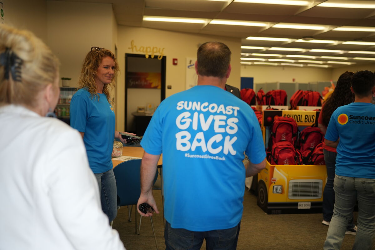 People in blue shirts gather near a school bus cutout filled with backpacks.