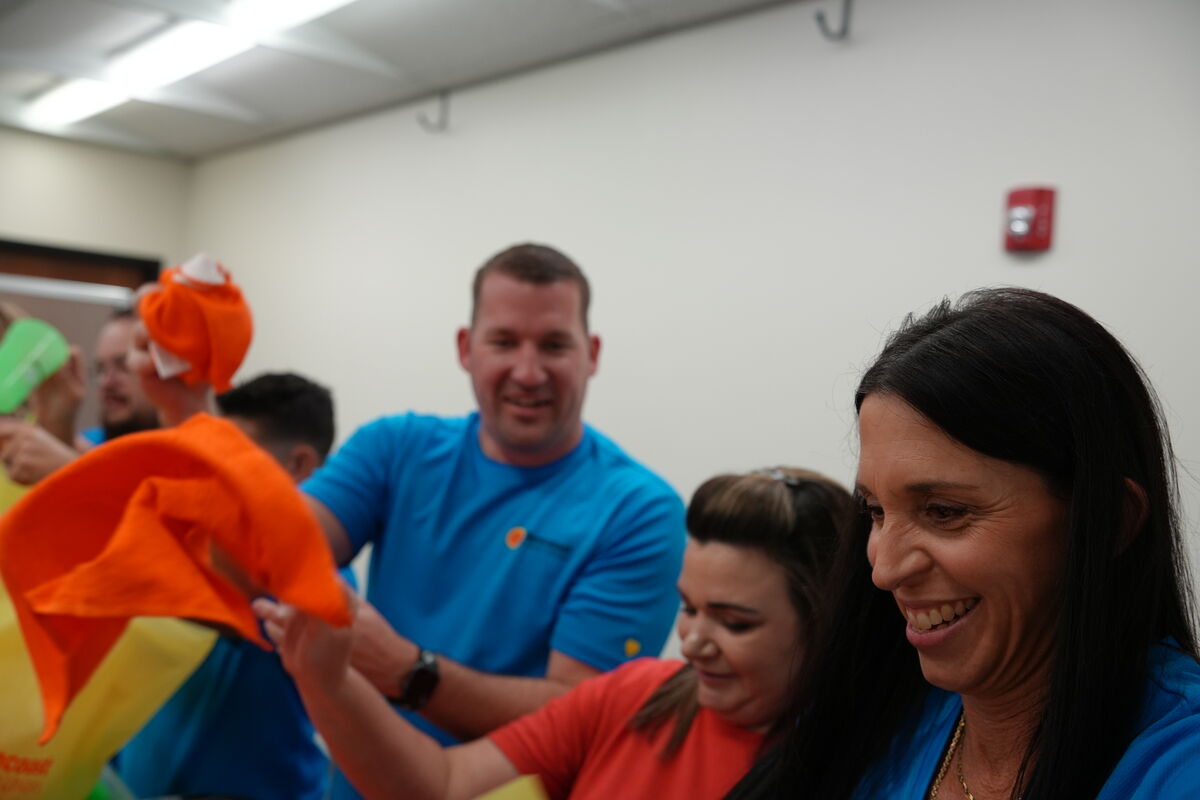A group of people smile and hold up orange and green items indoors.