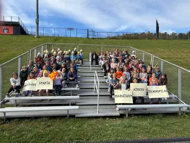 A large group of students pose on stadium steps, some wearing helmets.