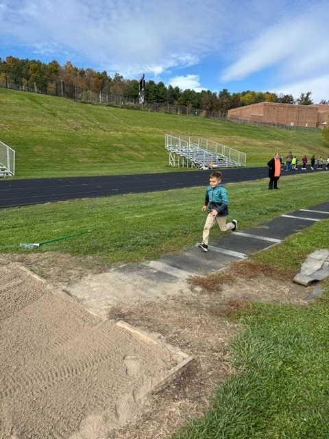 A young boy runs towards a long jump pit on a track field.