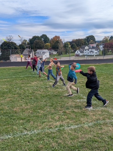 Children throw frisbees on a grassy field under a cloudy sky.