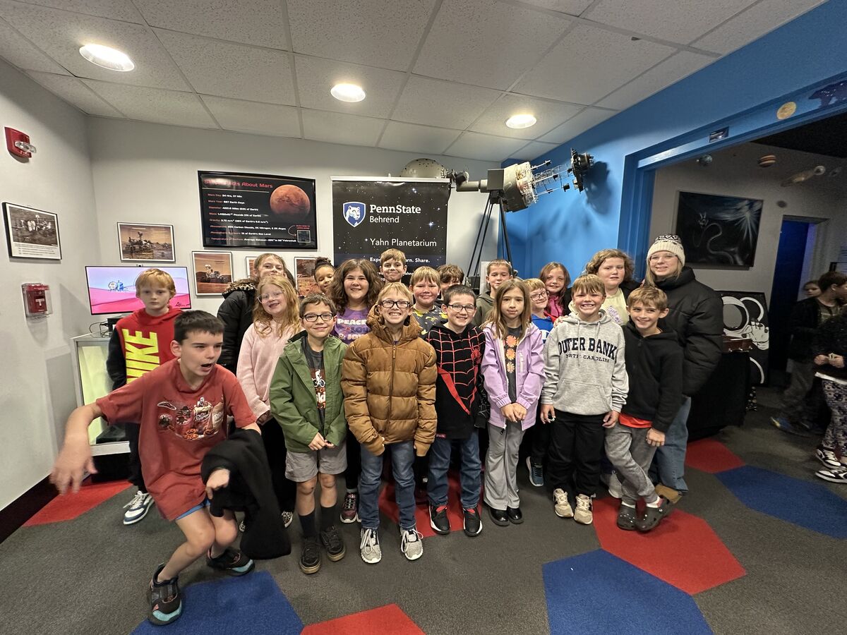 A group of children and adults pose for a photo inside a planetarium.