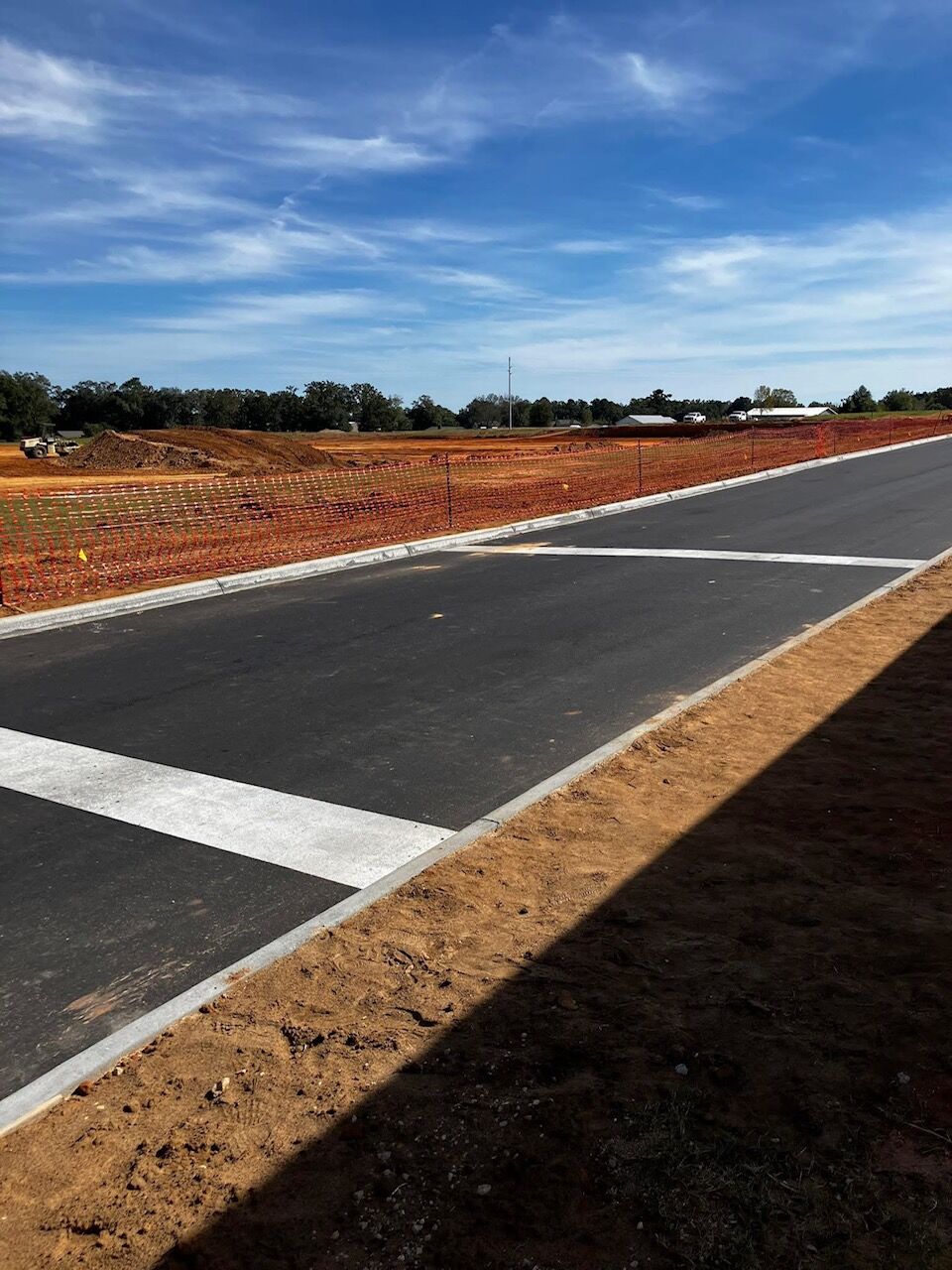 A newly paved road with white markings leads towards a construction site.